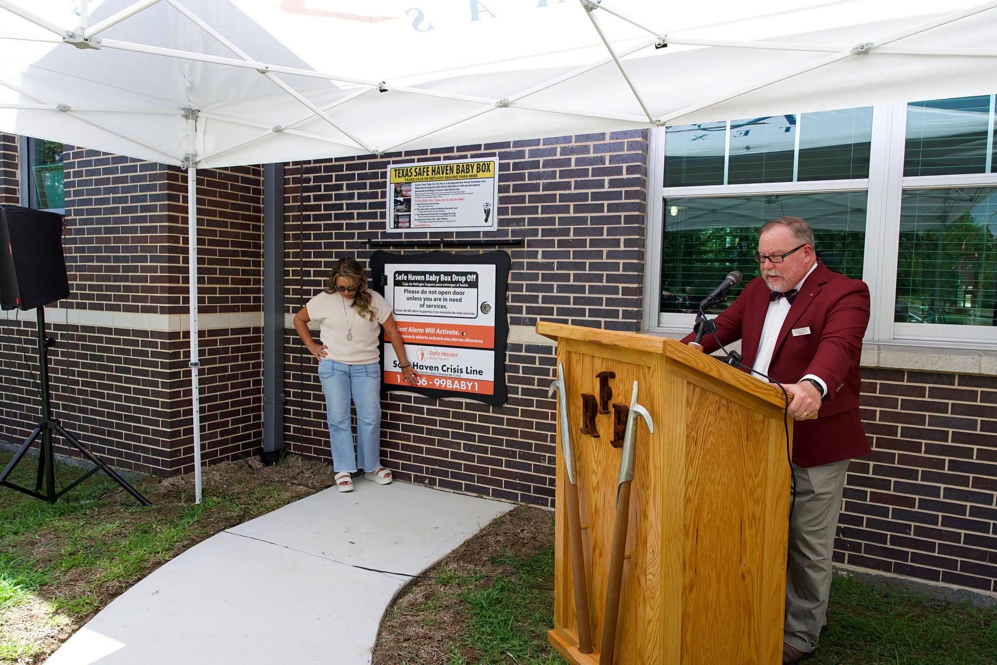 A speaker addressing the crowd at the dedication ceremony, next to the Safe Haven Baby Box drop-off door